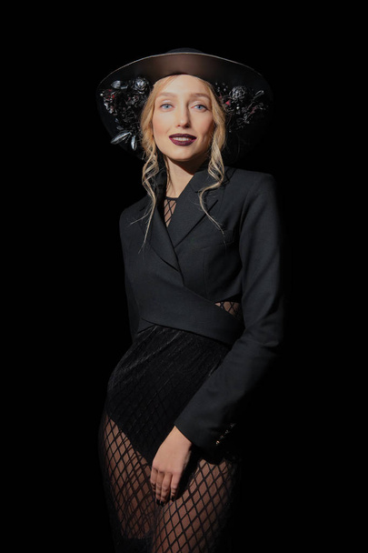 Sexy fashion model in fishnet dress and hat with flowers posing in dark environment - Fotó, kép