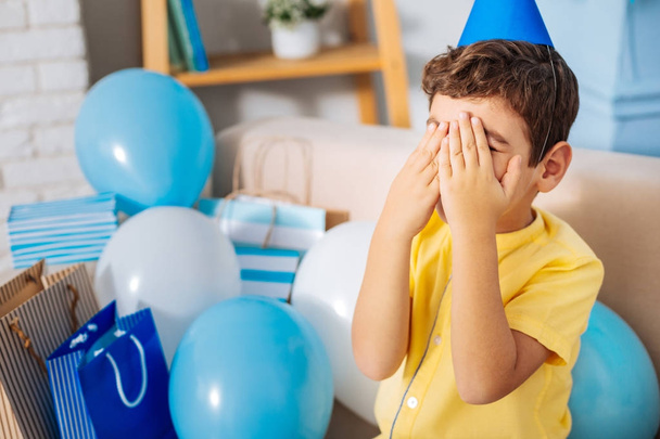 Pleasant boy waiting for birthday surprise while covering his eyes - Фото, изображение