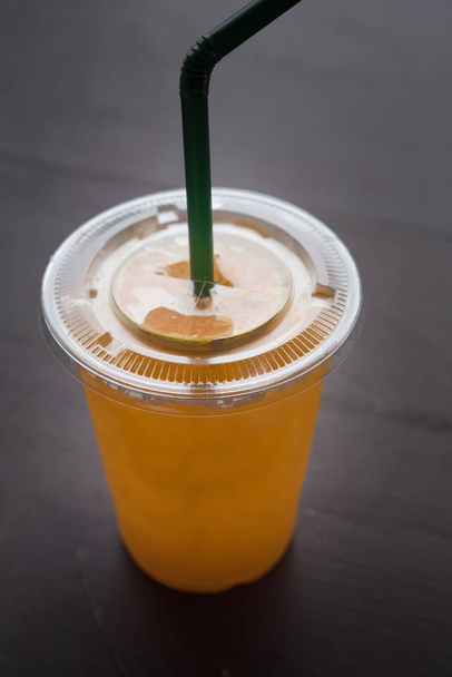 Χυμό πορτοκαλιού σε ένα πλαστικό ποτήρι τοποθετείται σε ένα ξύλινο τραπέζι. - Φωτογραφία, εικόνα