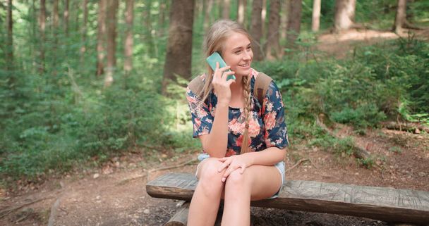 Νεαρή γυναίκα μιλάμε από το τηλέφωνο μέσα σε ένα δάσος. - Φωτογραφία, εικόνα