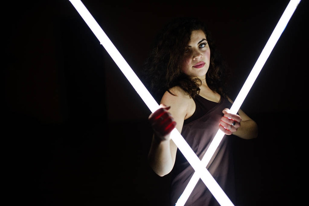 Curly brunette plus size model with two long led lamp at black r - Φωτογραφία, εικόνα