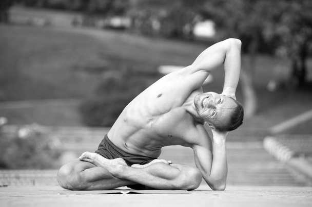 Athletic man doing yoga asanas in the park - Foto, afbeelding