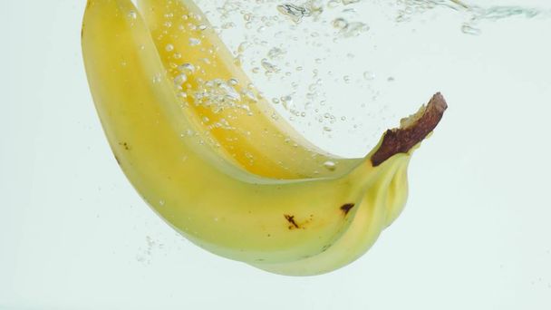 Bananas plunging into water on white background in slow motion - Фото, зображення