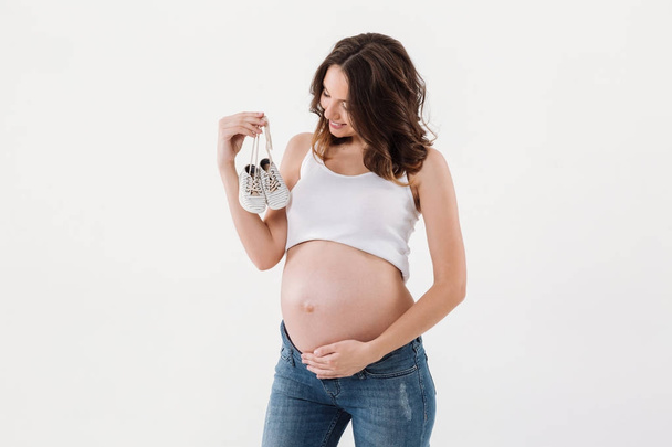 Szczęśliwa Kobieta w ciąży, trzymając małe buty dziecięce. - Zdjęcie, obraz