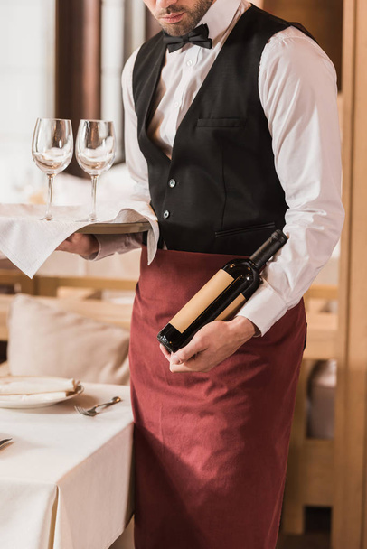 Camarero sosteniendo gafas de vino y botella
 - Foto, imagen
