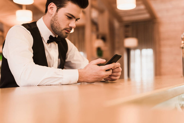 Waiter sitting at bar counter with smartphone - Foto, Imagem