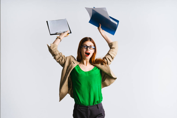 happy stylish girl with glasses, green jacket raised her hands up and holds documents - 写真・画像
