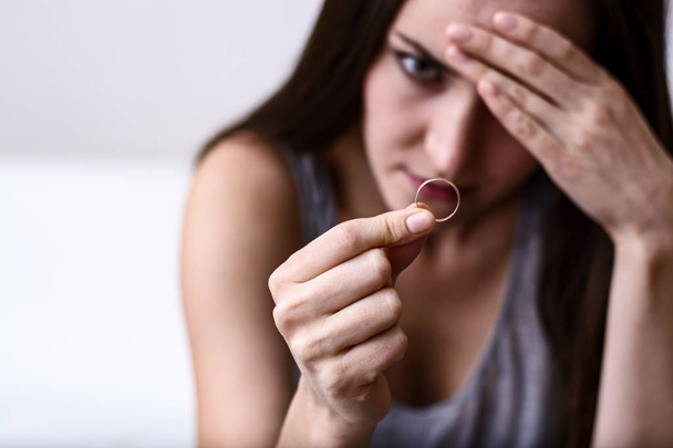 Naštvaná žena truchlí po rozvodu drží snubní prsten sedí na bílé pohovce. - Fotografie, Obrázek