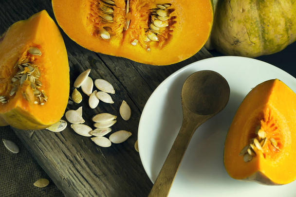Sliced ripe pumpkin in a white plate with seeds and a wooden spoon. Harvest. Autumn. - Photo, Image