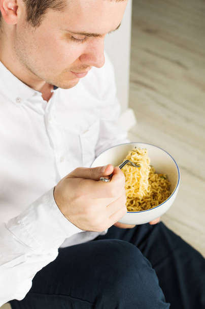 Young man is eating instant noodles from the white bowl - Foto, Imagem