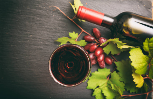 Copo de vinho tinto e garrafa e uvas frescas em fundo preto, foco no copo de vinho
 - Foto, Imagem