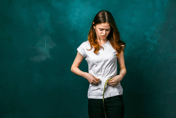 young sad girl in a white T-shirt measures the volume of her waistline - Fotoğraf, Görsel