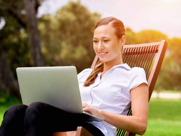 Young business woman sitting in park and working with laptop - Fotó, kép