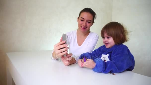 Młoda matka i córeczkę, grając z aparatu w telefonie, dziewczyny siedzi i za pomocą kamery śmieszne efekty. - Materiał filmowy, wideo