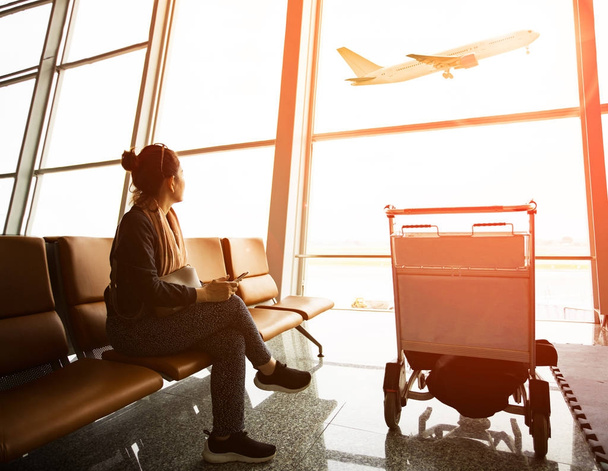 alleenstaande vrouw zitten in de luchthaventerminal en reizigerskilometers vliegtuig vliegen - Foto, afbeelding