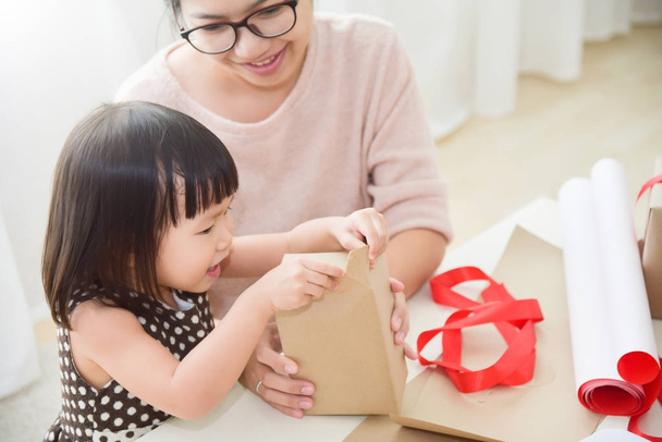 Young mother and her daughter wrapping a gift box. - Foto, afbeelding