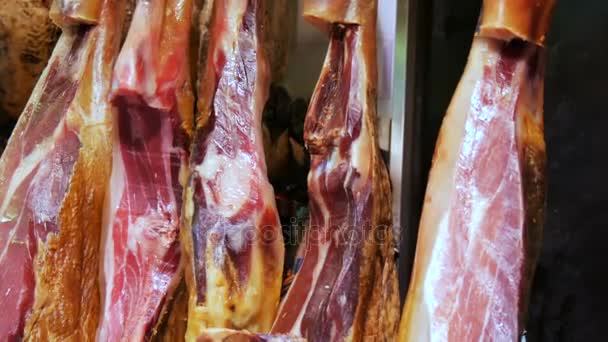 Dried pork thighs hang on the meat market counter. Spanish national dish of ham or jamon with streaks of fat - Footage, Video
