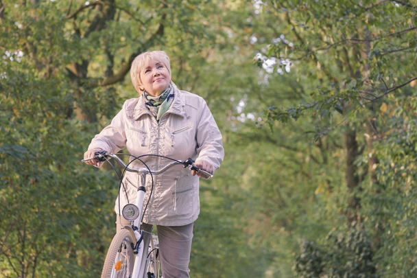 アクティブな幸せな屈託のない笑みを浮かべて年配の女性秋の自然の中自転車をなくし. - 写真・画像