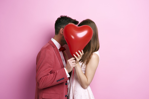 Affectionate couple covering face with balloon and kissing  - Fotografie, Obrázek