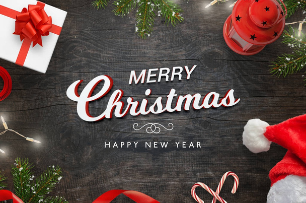 Χριστούγεννα Merr κείμενο σε μαύρο ξύλινο τραπέζι surrrounded με Χριστουγεννιάτικο δέντρο, είδη δώρων, γλυκά, φώτα, Αϊ Βασίλη καπέλο και φανάρι - Φωτογραφία, εικόνα