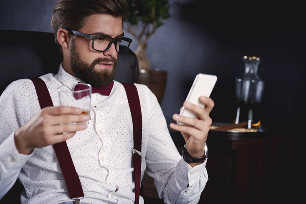 Businessman using his smartphone and drinking tea - Photo, Image