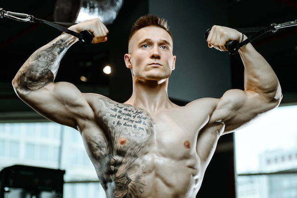 Handsome model young man training arms in gym - Foto, Bild