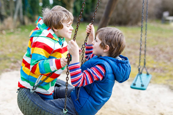 Two little kid boys having fun with chain swing on outdoor playground - Photo, Image