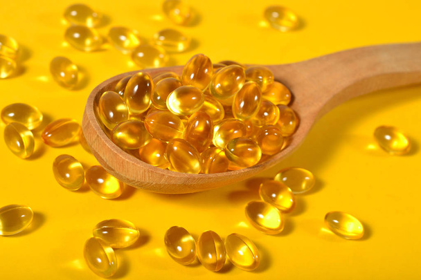 Omega-3 fish fat oil capsules in wooden spoon on a yellow - Foto, Imagem