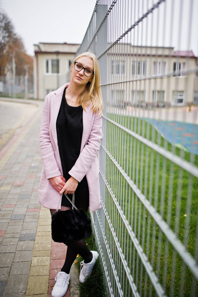 Blonde girl at glasses and pink coat, black tunic and handbag po - Фото, изображение