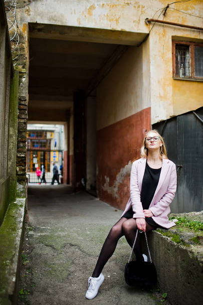 Blonde girl at glasses and pink coat, black tunic and handbag po - Foto, imagen