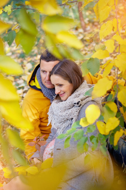 Pregnant woman and man relaxing at autumn park - 写真・画像