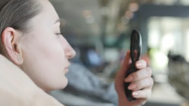 Νεαρή γυναίκα κοιτάζοντας στον καθρέφτη και διορθώνοντας τα μαλλιά της. Εσωτερικη ΠΕΡΙΠΟΙΗΣΗ ΜΑΛΛΙΩΝ - Πλάνα, βίντεο