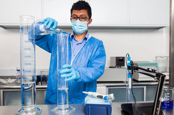 Νεαρά αρσενικά επιστήμονας που εργάζεται στο εργαστήριο ντυμένος με μπλε - Φωτογραφία, εικόνα