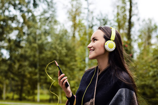 静かな公園でヘッドフォンとスマート フォンからの音楽を聴く若い幸せな女 - 写真・画像