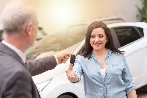 Prodavač aut předání klíče od auta k mladé ženě, světelný efekt - Fotografie, Obrázek
