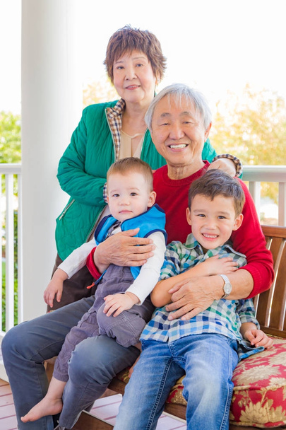 Старшая взрослая китайская пара, сидящая со своими внуками смешанной расы
 - Фото, изображение
