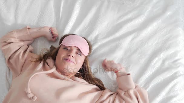 Mujer lleva máscara de sueño en la cama, atractiva mujer bastante caucásica bosteza en la cama, la chica se está estirando, la preparación para el sueño, el sueño diurno y la relajación
 - Imágenes, Vídeo