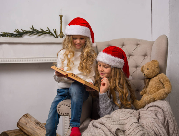 Két kislány sapkák Santa olvasod, egy könyvet a armchai - Fotó, kép