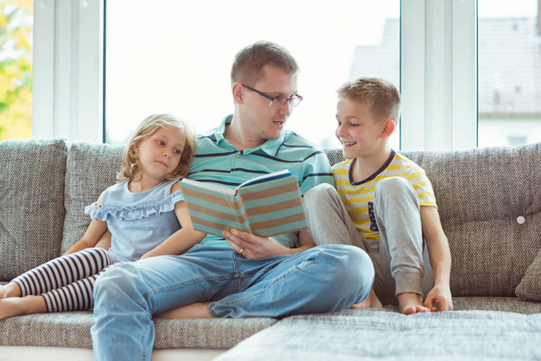 Young happy father reading book with cute children at home - Φωτογραφία, εικόνα