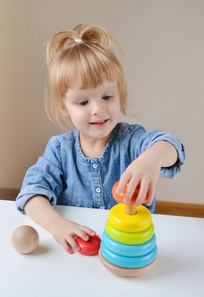 Suloinen pieni valkoinen tyttö leikkii puinen värikäs lelu pyramidi
  - Valokuva, kuva