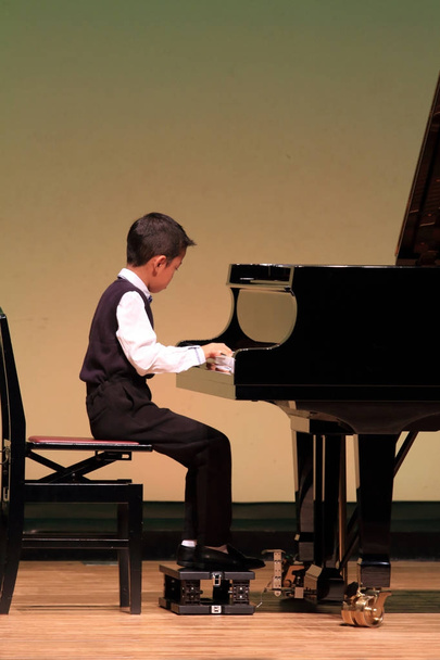 Японский мальчик играет на фортепиано на сцене (второй класс начальной школы
) - Фото, изображение
