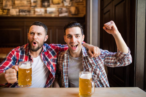Dwóch mężczyzn przed telewizorem z piwem radować się zwycięstwo swojej ulubionej drużyny w pubie - Zdjęcie, obraz