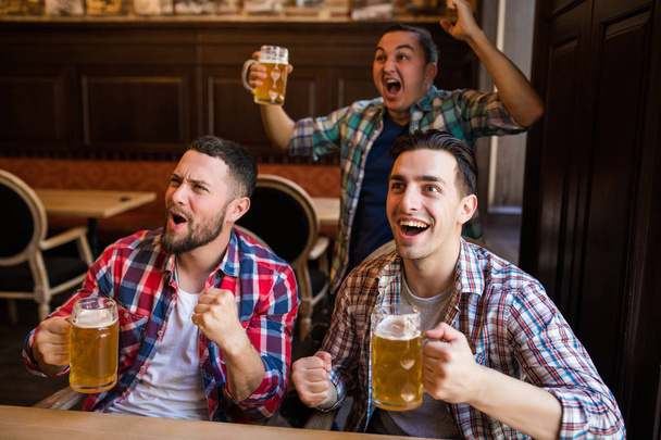 happy football fans or male friends drinking beer and celebrating victory at bar or pub - Photo, Image