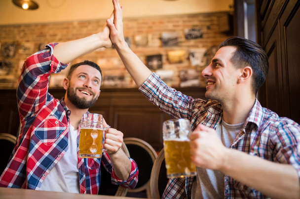 glücklicher junger bärtiger Mann, der seinen Freund beim gemeinsamen Bier in der Kneipe hochlachend verfünffacht - Foto, Bild