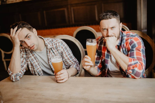 Young bearded man looking upset and sad having beer at the pub copyspace depression stress tired exhausted crisis drinking problems issues unhappy disappointment regret sadness loneliness alcohol - Photo, image