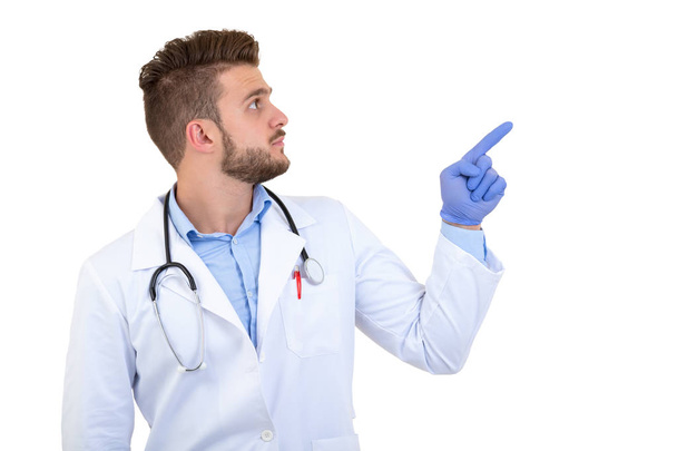 Portrait of a Young smiling male doctor pointing finger away isolated on a white background - Foto, Bild