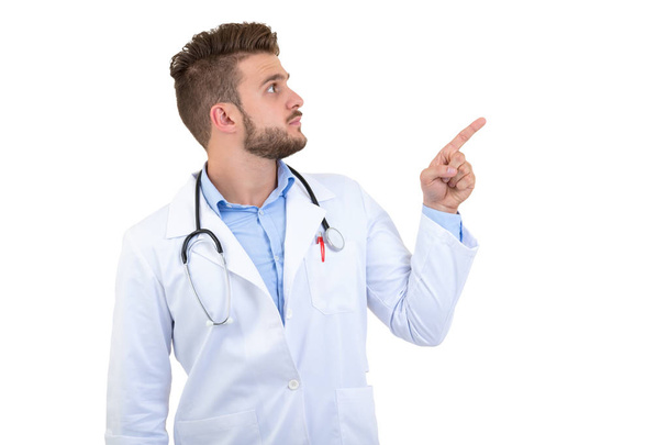 Retrato de un joven sonriente doctor señalando con el dedo aislado sobre un fondo blanco
 - Foto, imagen