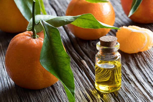 A bottle of tangerine essential oil with tangerines in the backg - Valokuva, kuva
