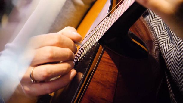 Closeup mooie akoestische gitaar bespeeld door vrouw zitten, musicus concept. Vrouw spelen van de gitaar-closeup - Foto, afbeelding