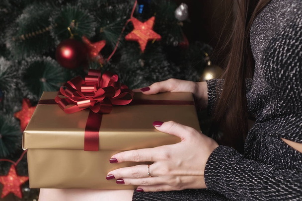 ein Mädchen hält ein Geschenk in der Hand und sitzt unter einem Weihnachtsbaum - Foto, Bild